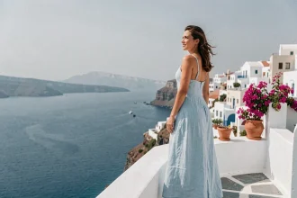 Voyageuse en robe de lin sur une terrasse blanche à Folégandros avec vue sur la mer Égée